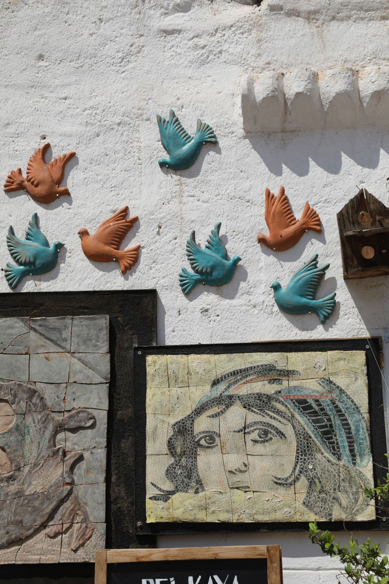 Ceramic birds, reminiscent of things to do in Avanos, Cappadocia, mounted on a white wall above an artwork featuring a woman's face, under bright sunlight.