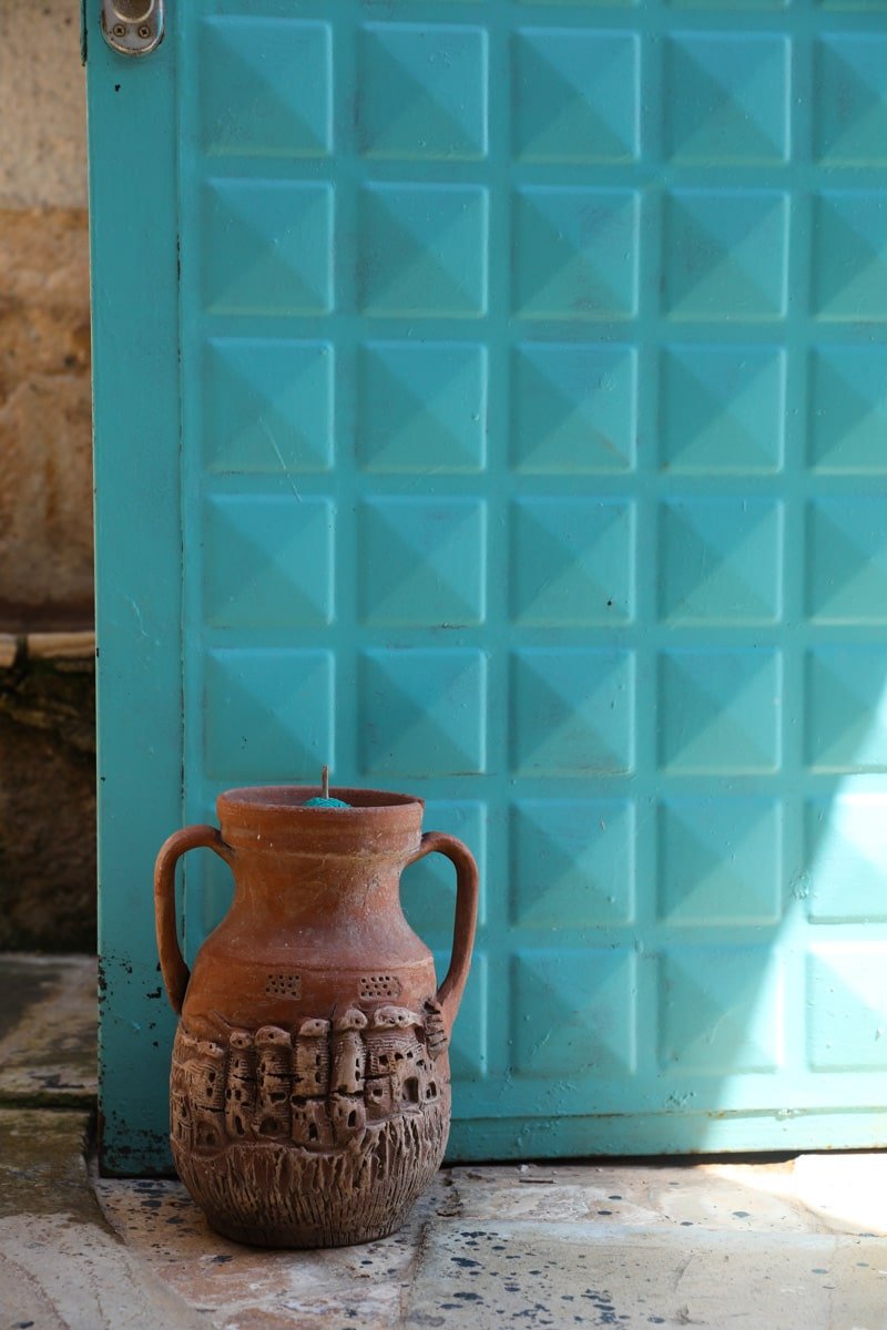 A terracotta jug, a typical craft from Avanos, Cappadocia, is placed beside a turquoise door with a geometric pattern.