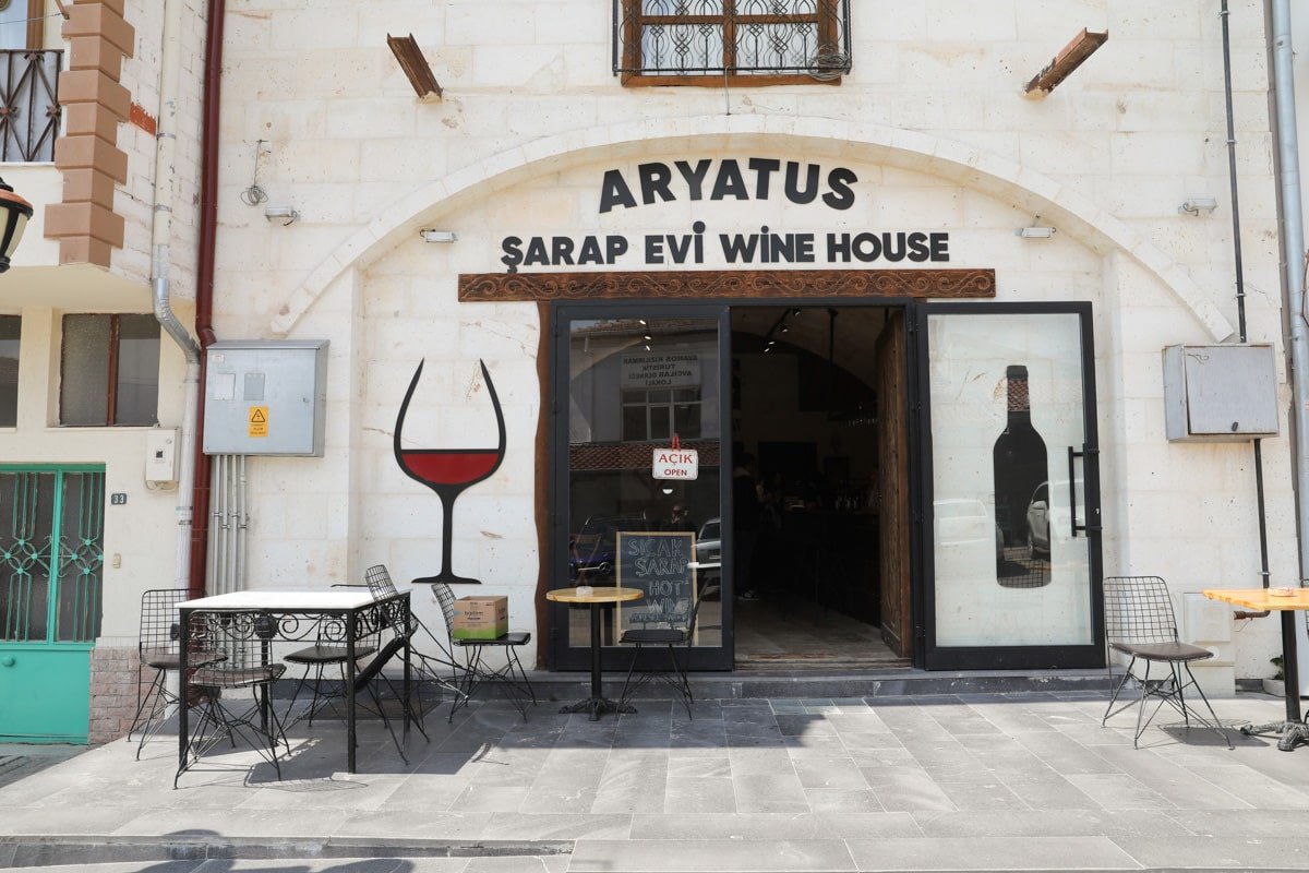 Front entrance of Aryatus Wine House in Avanos, Cappadocia, Turkiye, with tables and chairs outside, wine glass and bottle signs above the door.