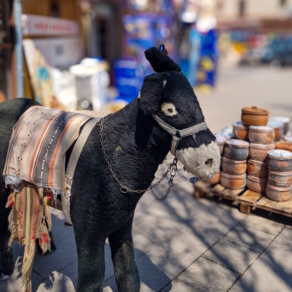 A life-sized model of a donkey wearing a traditional blanket and harness, displayed on a street with pottery in the background, is one of the intriguing things to do in Avanos Cappadoc