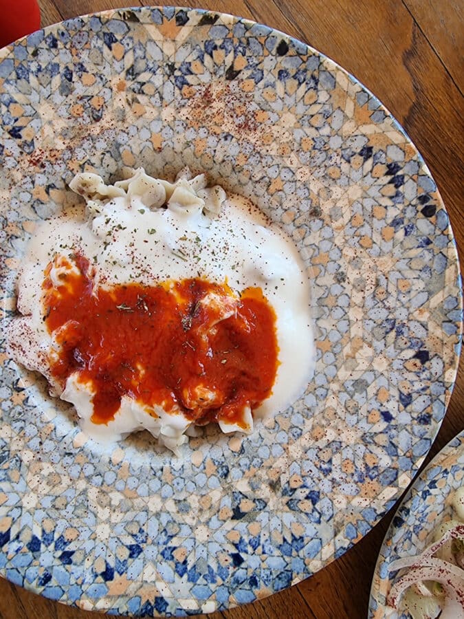 A plate of turkish manti garnished with yogurt and red pepper sauce, sprinkled with spices, on a mosaic-patterned plate in Avanos Cappadoccia Turkiye.