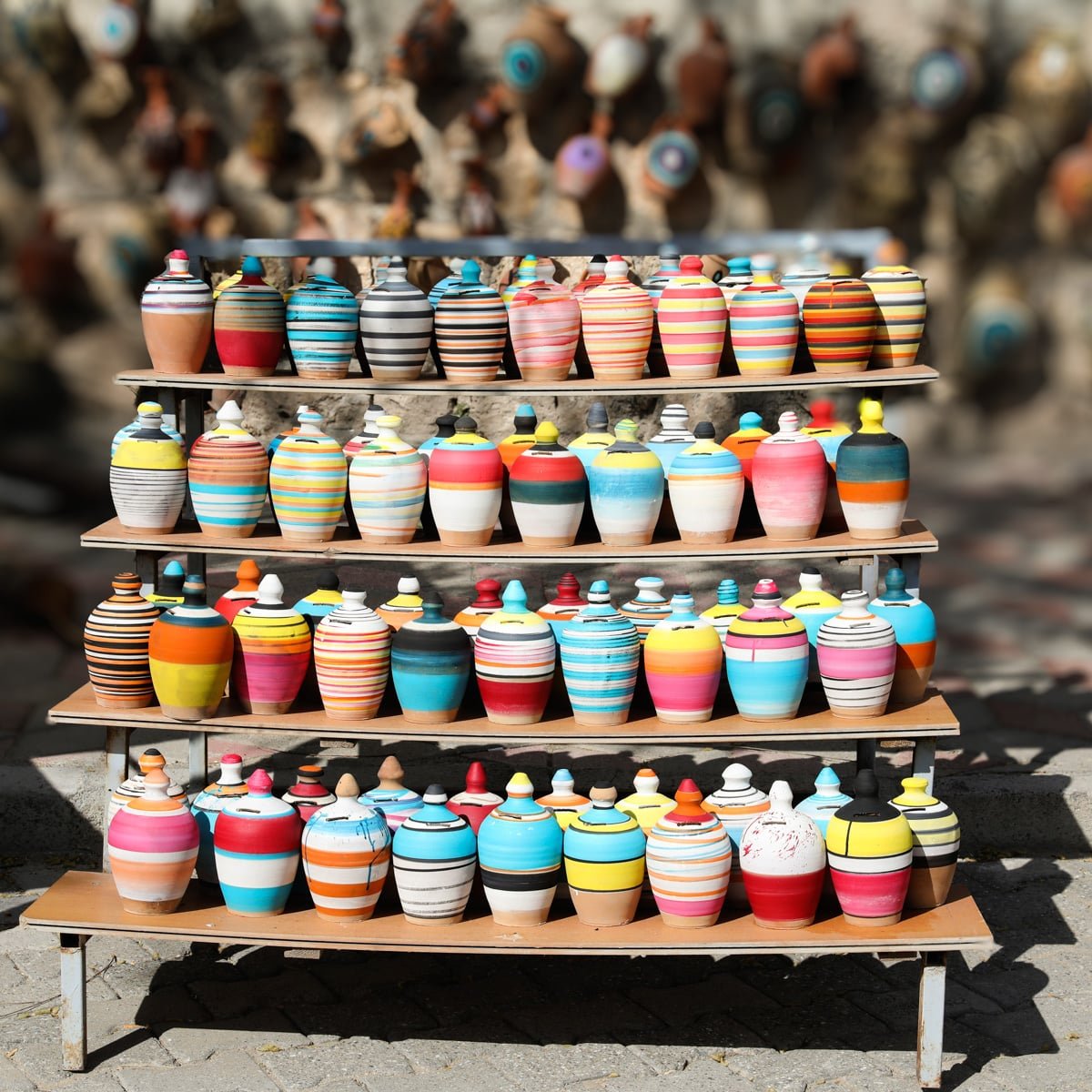 A display of colorful, striped ceramic pots on wooden shelves, arranged in a sunny outdoor market setting, showcasing things to do in Avanos, Cappadocia, Turkey.