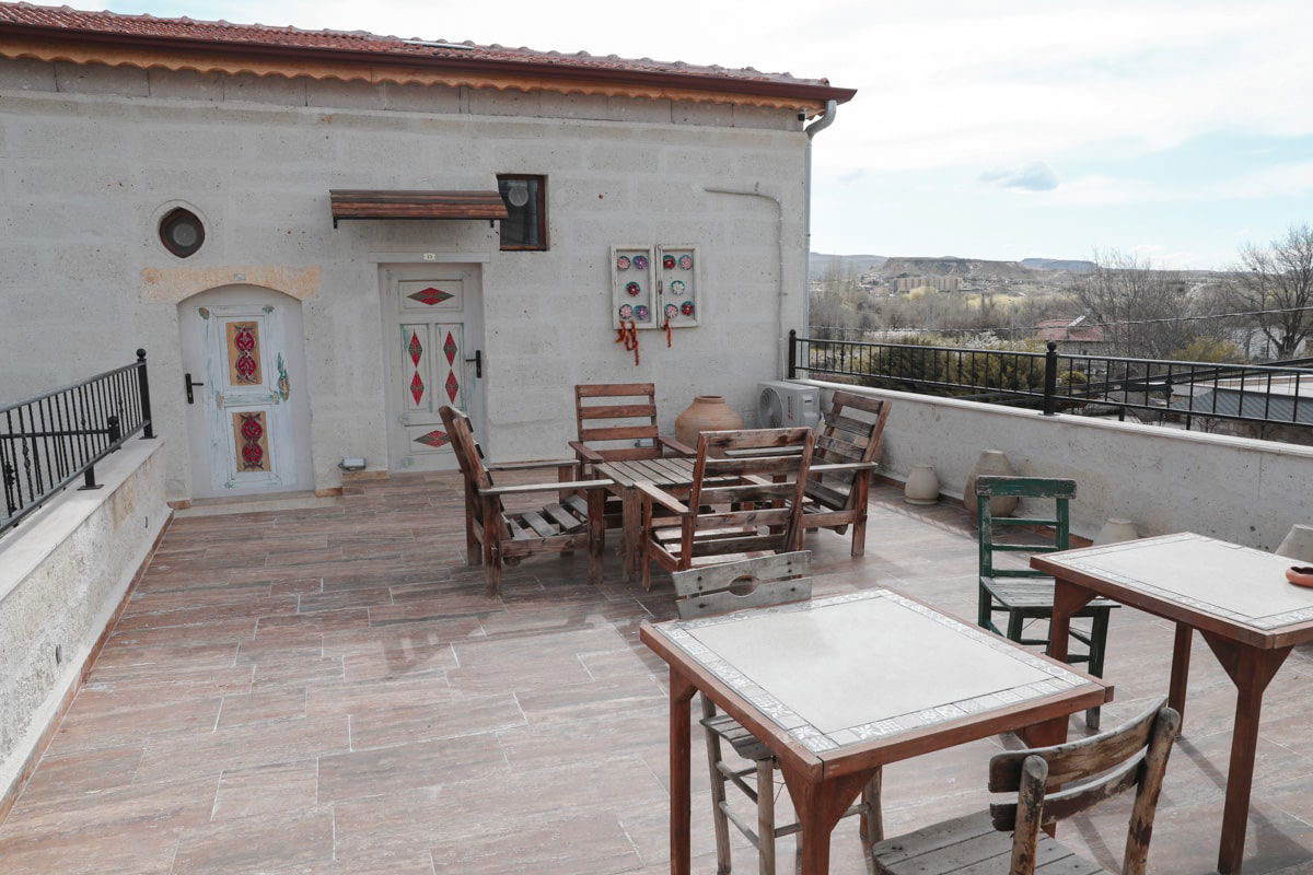 Patio with traditional stone walls, adorned with colorful flags, featuring wooden furniture and scenic distant hills, offers a glimpse of things to do in Avanos Cappadocia, Turkiye.