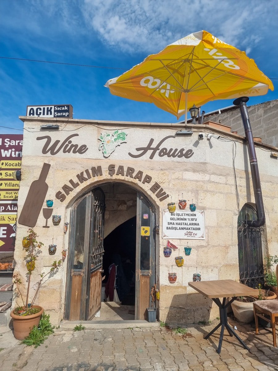 Entrance of "salkım sarap evi" wine house in Avanos Cappadocia, Turkey, featuring a yellow umbrella, decorative signage, and rustic adornments under a clear