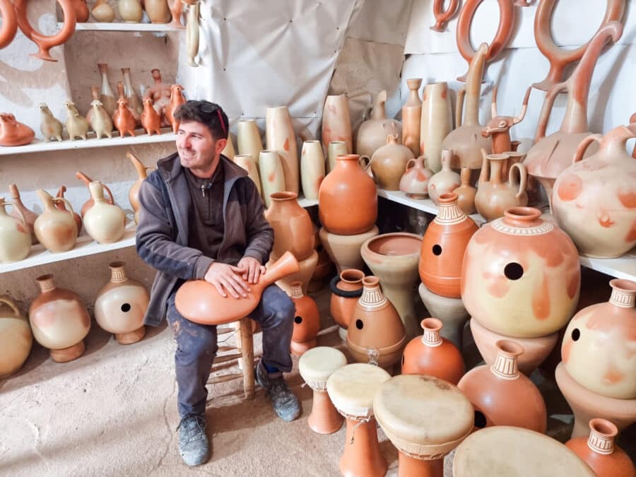 A man sits on a stool surrounded by traditional clay pottery in various shapes and sizes in a workshop, showcasing things to do in Avanos, Cappadocia, Turkey.