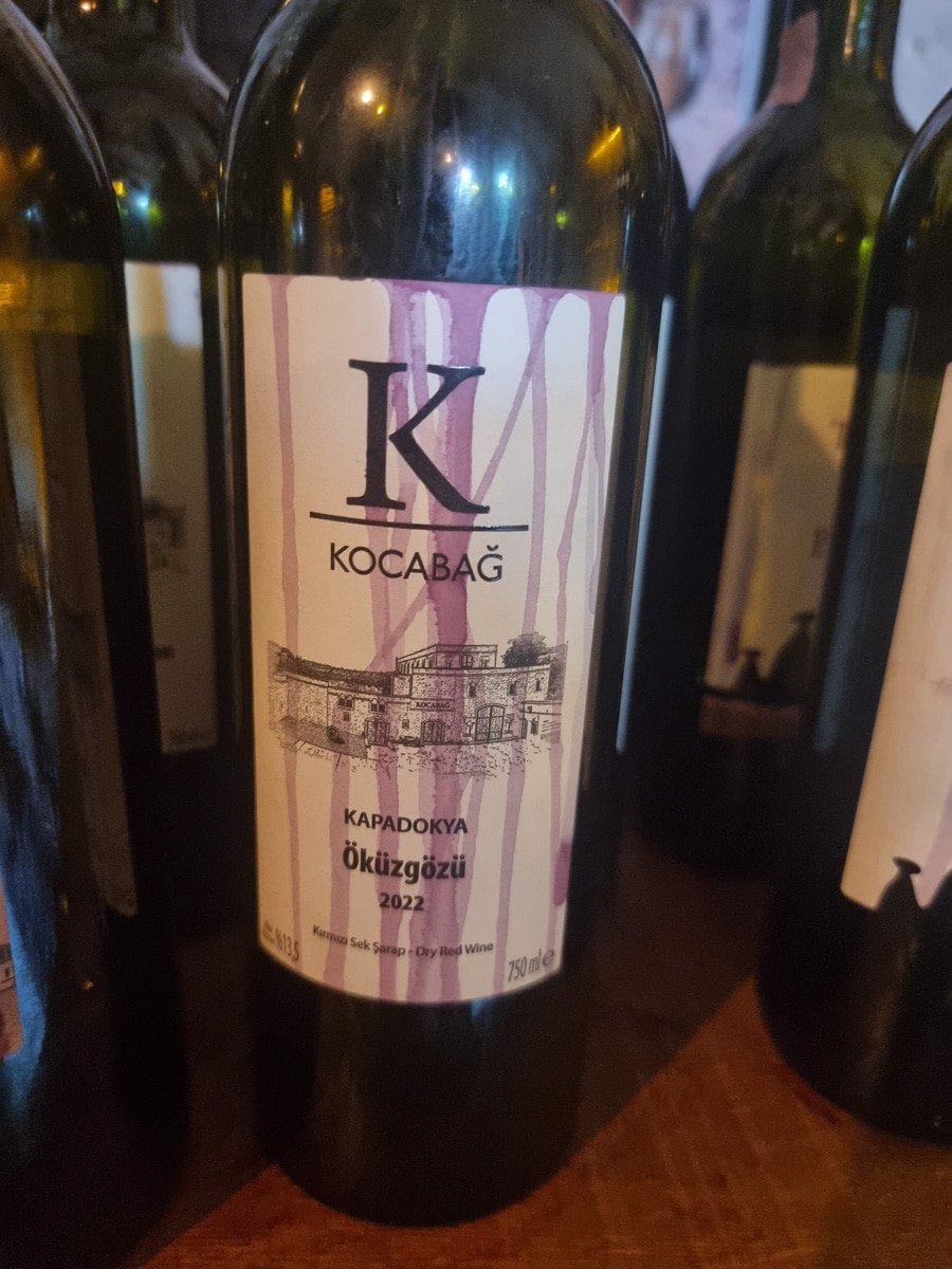 Close-up of a kocabağ wine bottle label, featuring the kapadokya logo, vintage year 2022, and background of other bottles in Avanos Cappadocia,