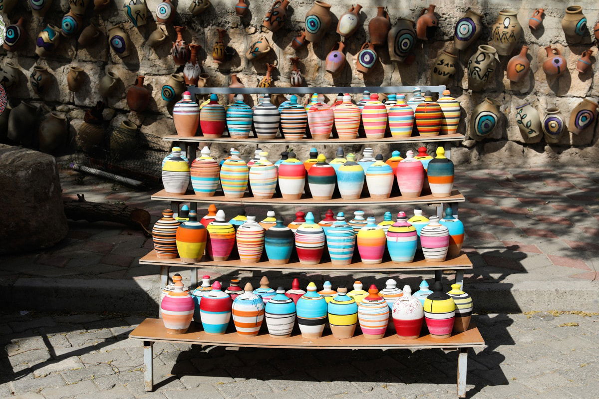 Colorful ceramic pots in various sizes displayed on wooden shelves outdoors, showcasing the traditional craftsmanship of Avanos, Cappadocia, Turkiye.