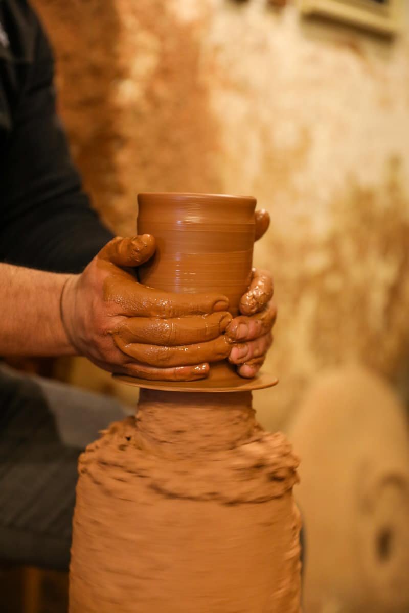 A potter's hands shaping a clay pot on a spinning pottery wheel, with focus on the wet, muddy texture of the clay. This is one of the many artistic things to do in Avanos