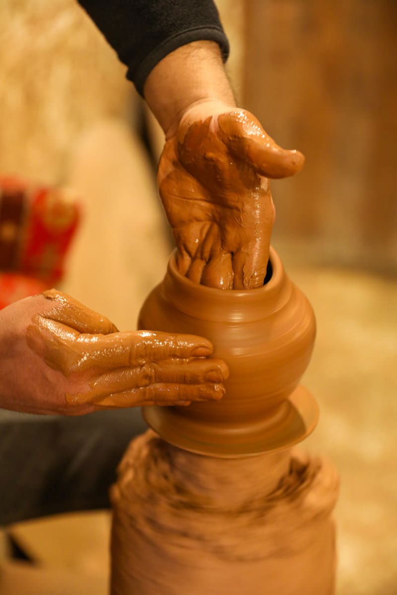 A potter's hands shaping wet clay on a spinning pottery wheel in Avanos, Cappadocia, with detailed focus on the muddy texture and hand movements.