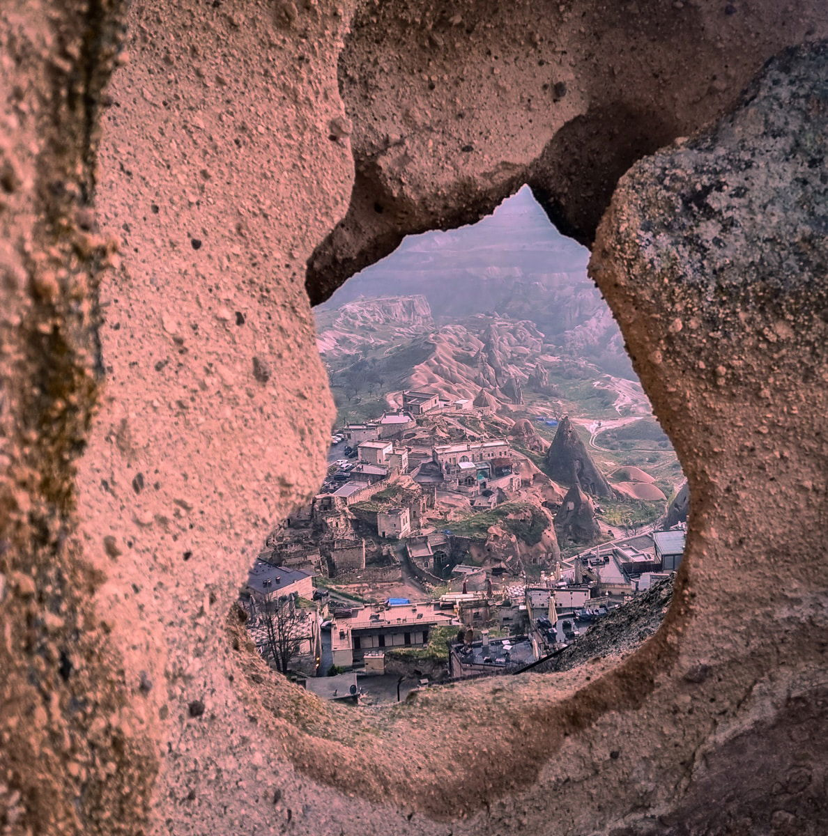 View of a village and mountainous landscape through Ushisar Castle's irregular-shaped hole in Cappadocia.