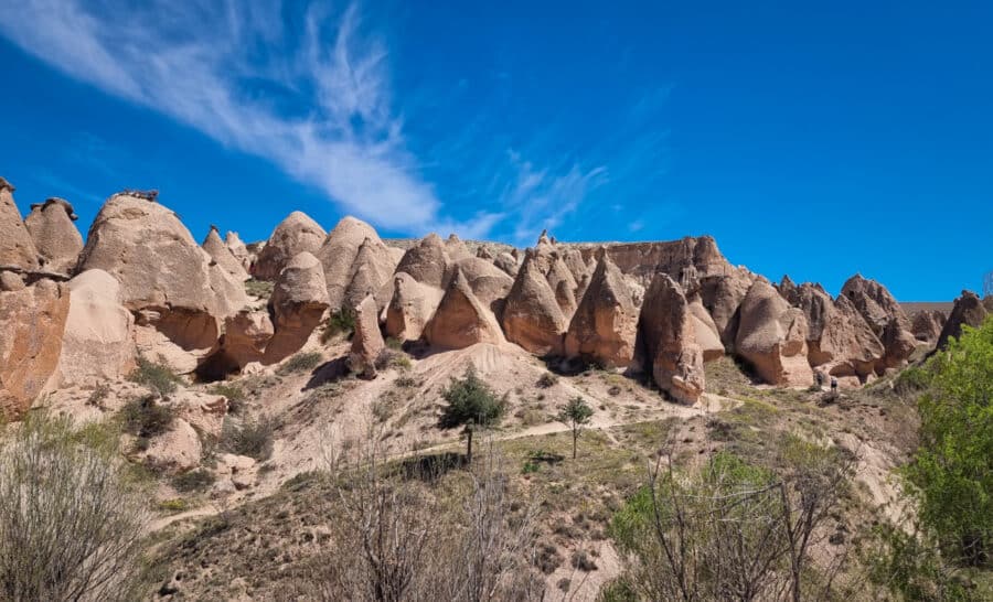 Panoramic view of unique, pointed rock formations under a blue sky with scattered clouds in Devrent Imagination Valley, Cappadocia, Turkey.