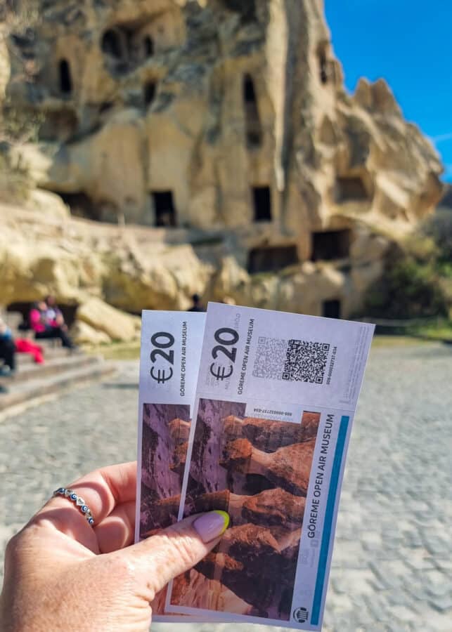 A person holding two 20 euro tickets with QR codes in front of the cave dwellings at the Goreme Open Air Museum, Cappadocia, Turkey.