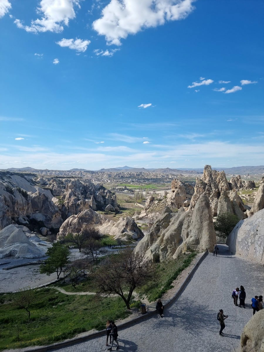 Scenic view of rocky landscape near Goreme Open Air Museum in Cappadocia with people walking on a pathway under a clear blue sky.