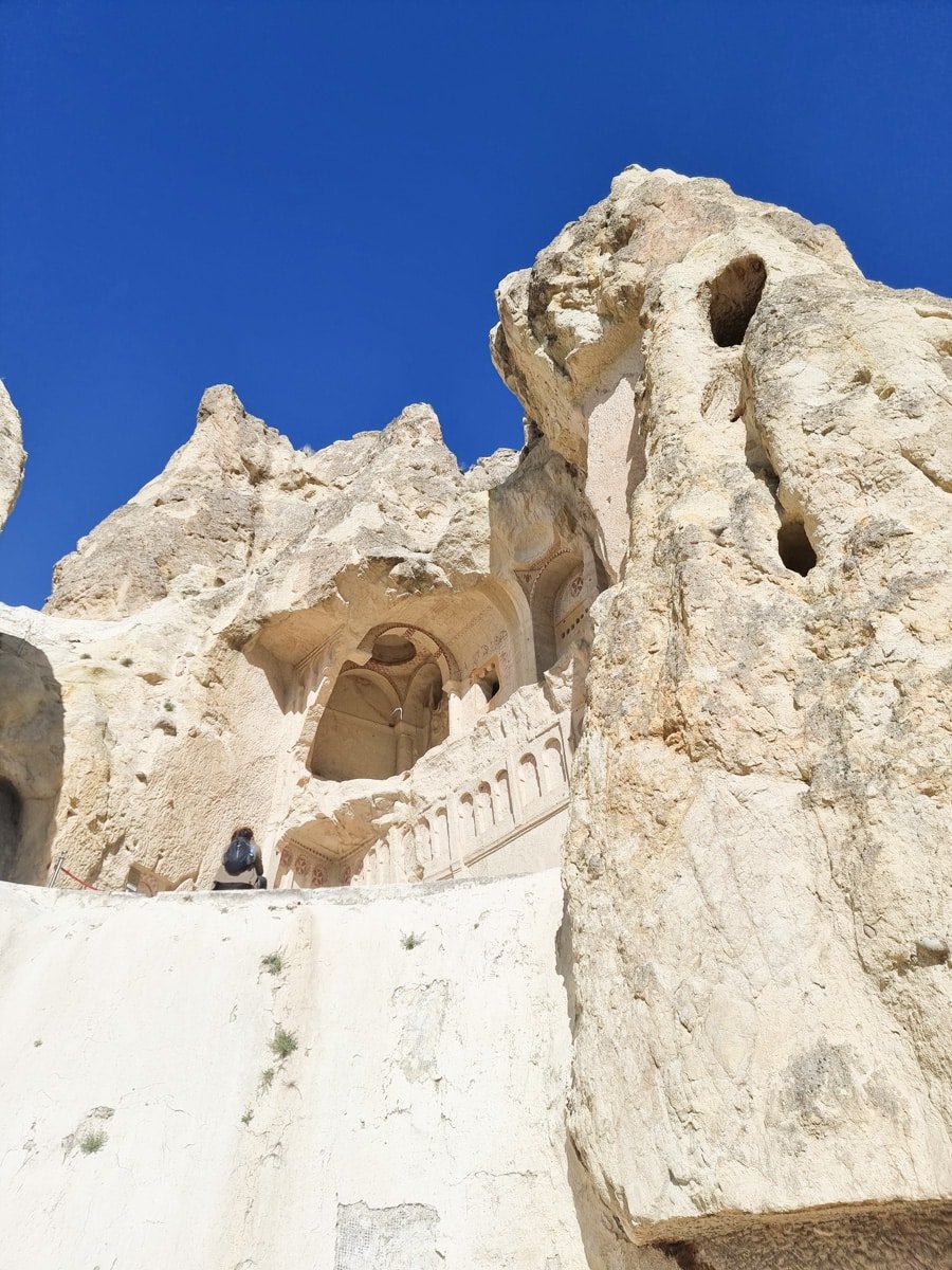 Ancient cave church with arched entrance carved into a rocky cliff under a clear blue sky at Goreme Open Air Museum in Cappadocia, Turkey.