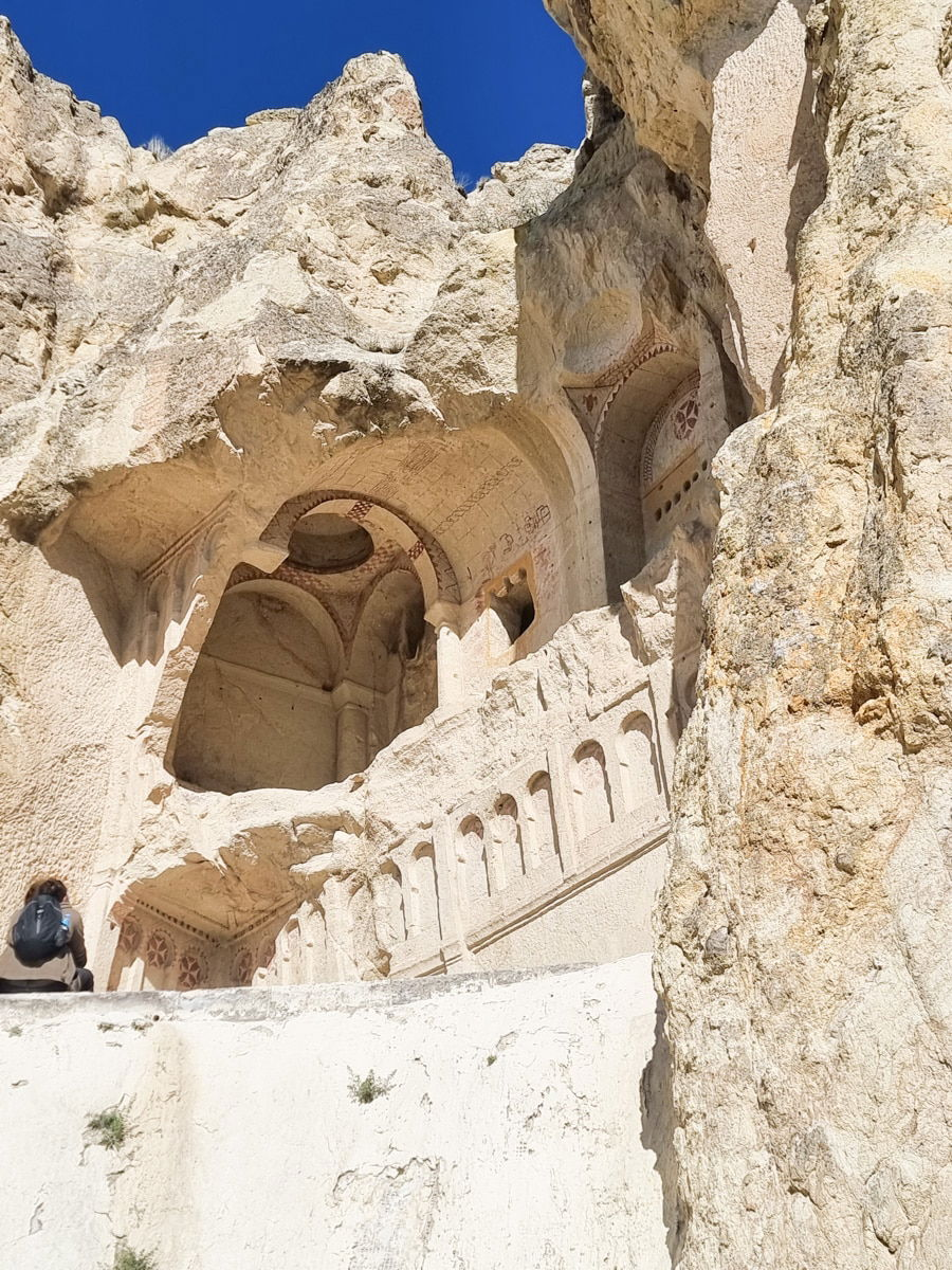 View of an ancient cave church at Goreme Open Air Museum, carved into a rocky hillside, showcasing detailed architectural elements and frescoes, under a clear blue sky.