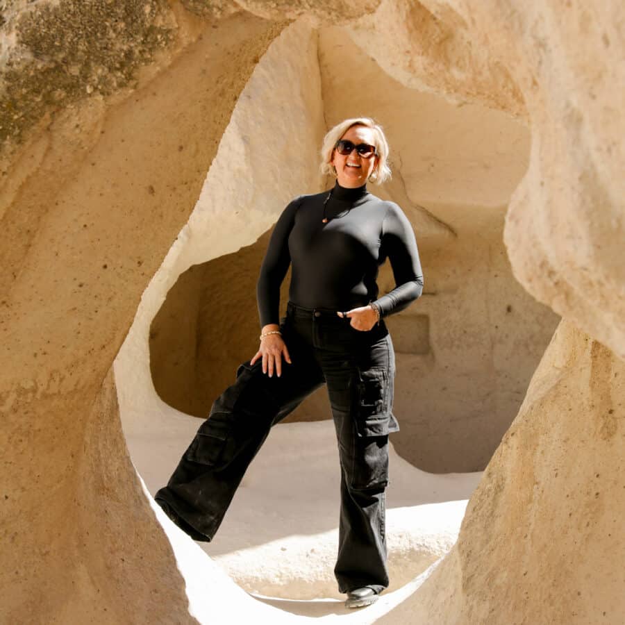 A woman in a black outfit standing in a natural archway carved into the sandy rock of Pasabag Valley, Cappadocia.