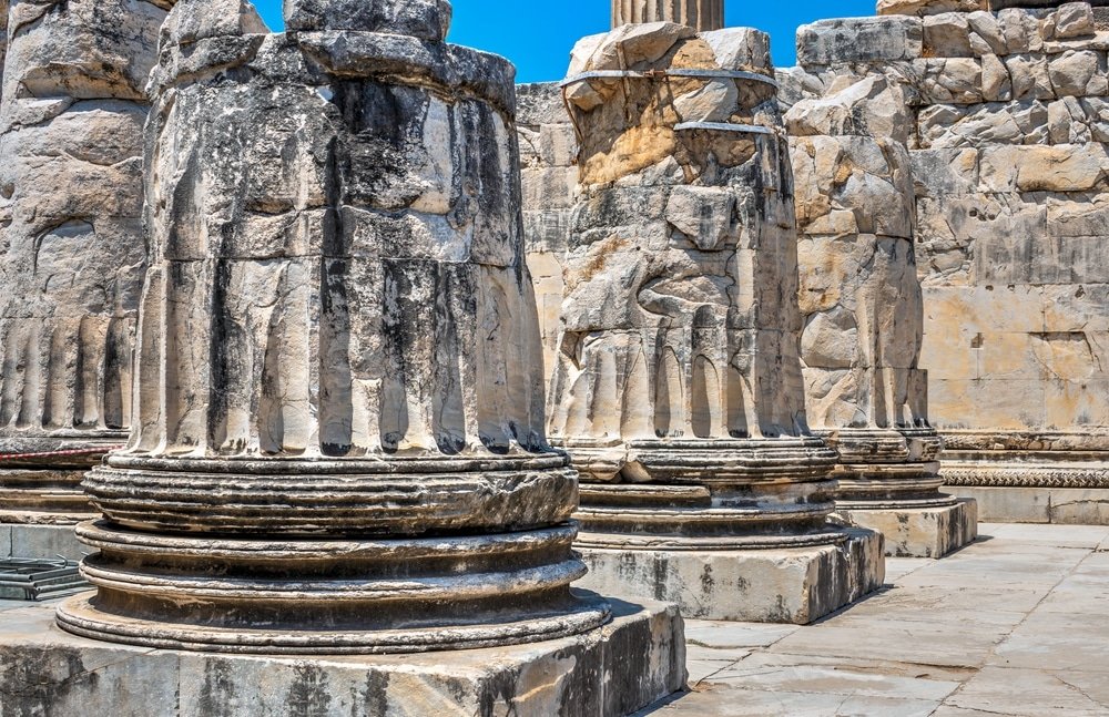 Ancient stone columns and carved reliefs at a historical ruin site in Aydın Province under a clear blue sky.
