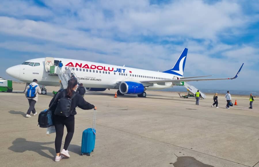 Passengers walking towards a parked AnadoluJet airplane, a subsidiary of Turkish Airlines, on a cloudy day at an airport tarmac in Turkey.