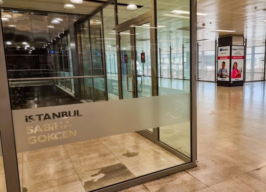 Glass doors with the logo of Istanbul Sabiha Gokcen Airport, leading visitors into a brightly lit interior passage of Turkey's transport hub.