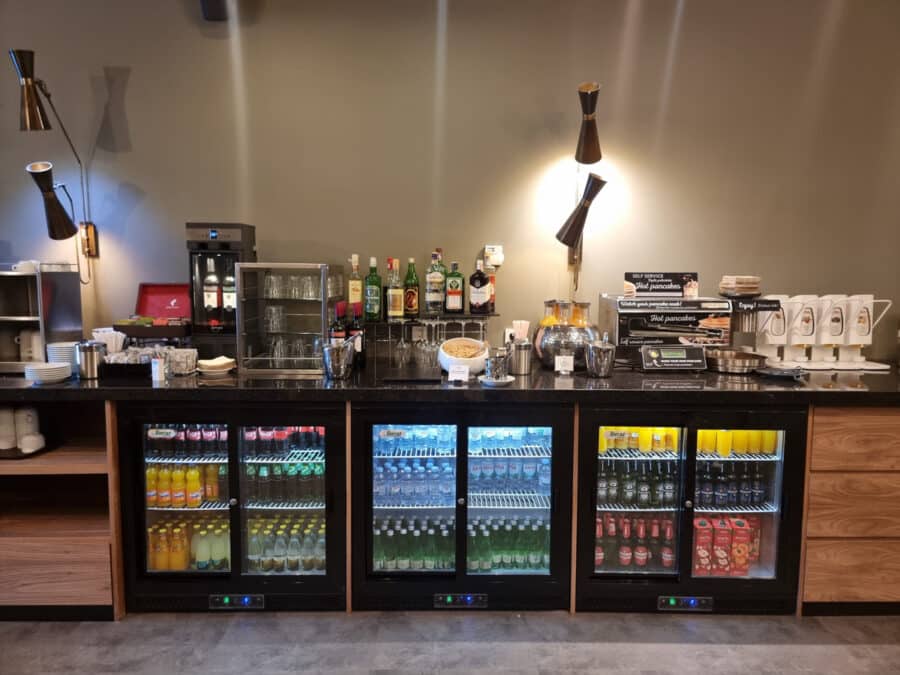 A well-organized hotel beverage station featuring refrigerated drinks, assorted liquors, and neatly arranged coffee cups under soft lighting, with the addition of Turkey transport information conveniently displayed.