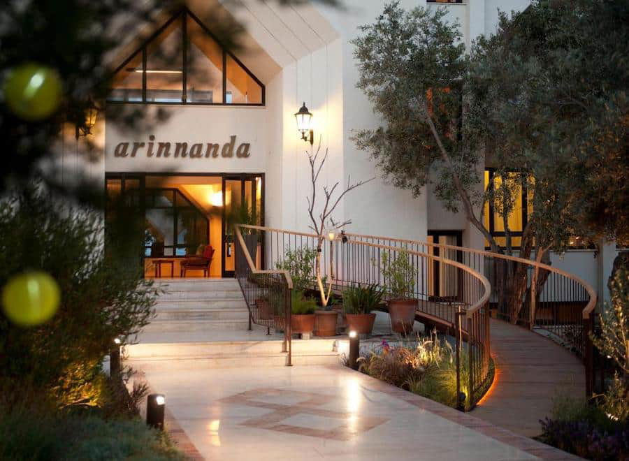 Evening view of a modern Cesme hotel entrance with a sign reading "arinanda," surrounded by tasteful landscaping and outdoor lighting.