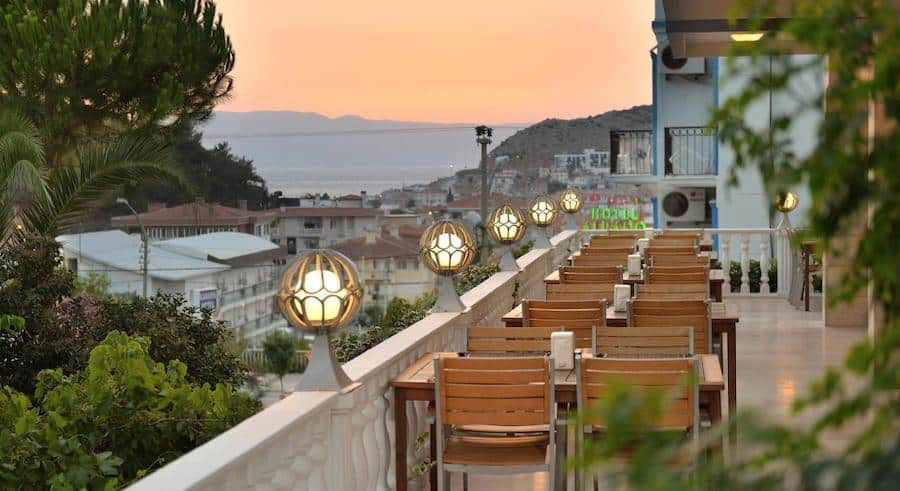 Outdoor restaurant terrace with wooden chairs and lit spherical lanterns, overlooking a coastal view at sunset in Çeşme.