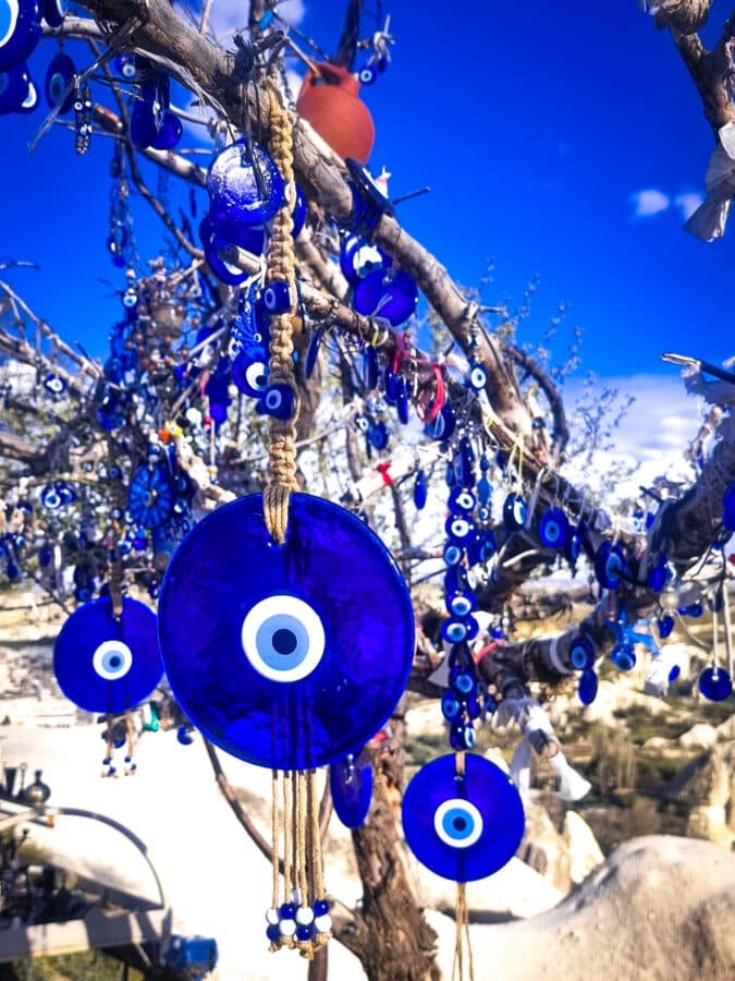Tree adorned with numerous blue evil eye amulets under a clear blue sky in Goreme, Cappadocia.