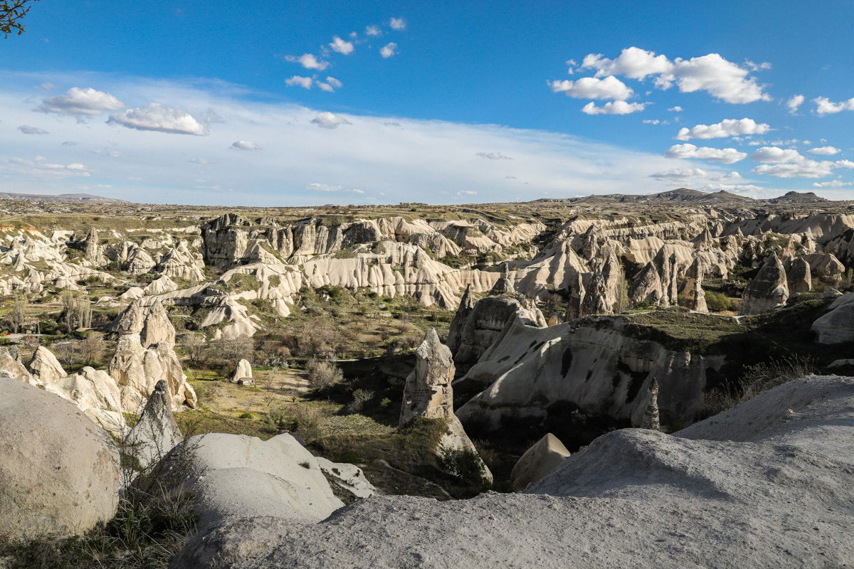 Panoramic view of Goreme's rugged landscape featuring distinctive rock formations and valleys under a partly cloudy sky.