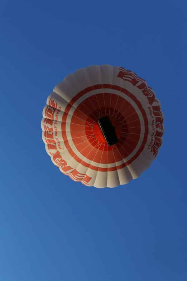 A red and white hot air balloon with intricate designs floats against a clear blue sky in Cappadocia.