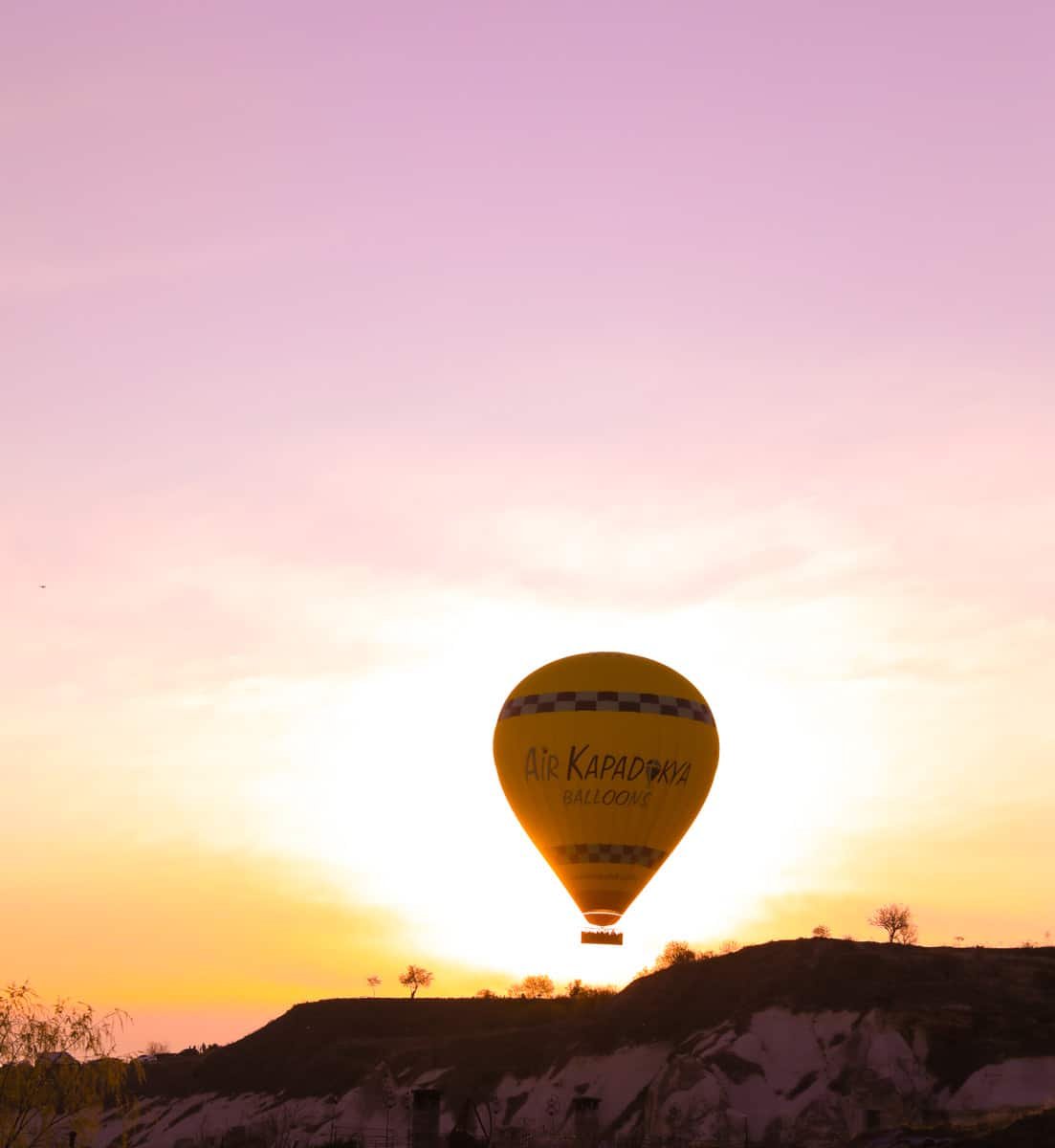 A hot air balloon floats in a pastel-hued sky during sunset, marked with the text "How To Spend 3 Days In Cappadocia".
