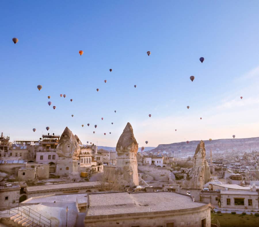 How To Spend 3 Days In Cappadocia: Hot air balloons floating above a rocky landscape with unique geological formations and buildings at sunrise.