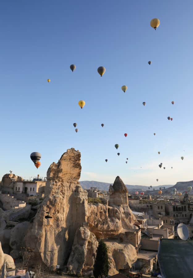 Hot air balloons soar above unique rock formations and buildings in Cappadocia, Turkey, under a clear blue sky, showcasing how to spend 3 days in this stunning location.