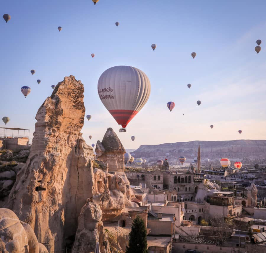 Hot air balloons float over the unique rock formations and town of Cappadocia, Turkey during sunrise, perfectly illustrating how to spend 3 days in Cappadocia with clear skies and
