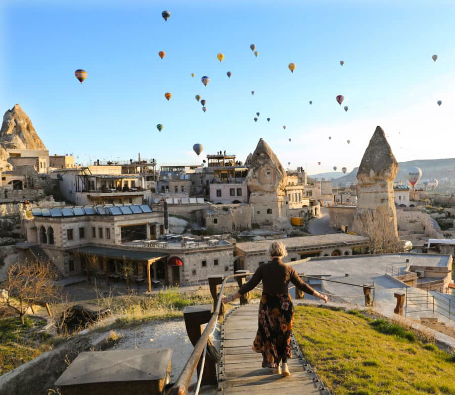 Woman walking down a staircase in Cappadocia, Turkey, with numerous hot air balloons floating in the sky above scenic rocky landscapes and traditional buildings, illustrating how to spend 3 days in C