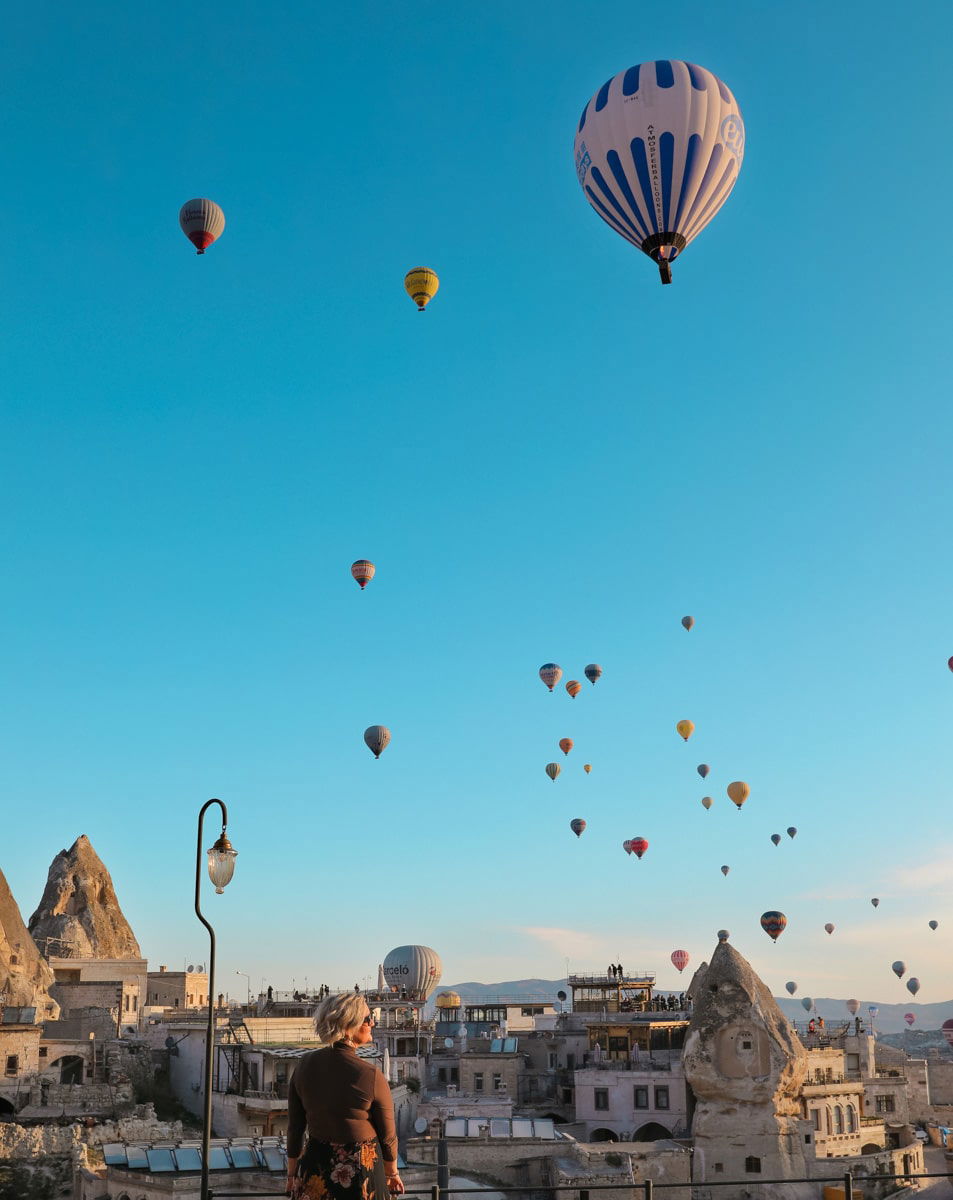 SJ watches numerous colorful hot air balloons soaring over a rocky landscape at sunrise in Cappadocia.