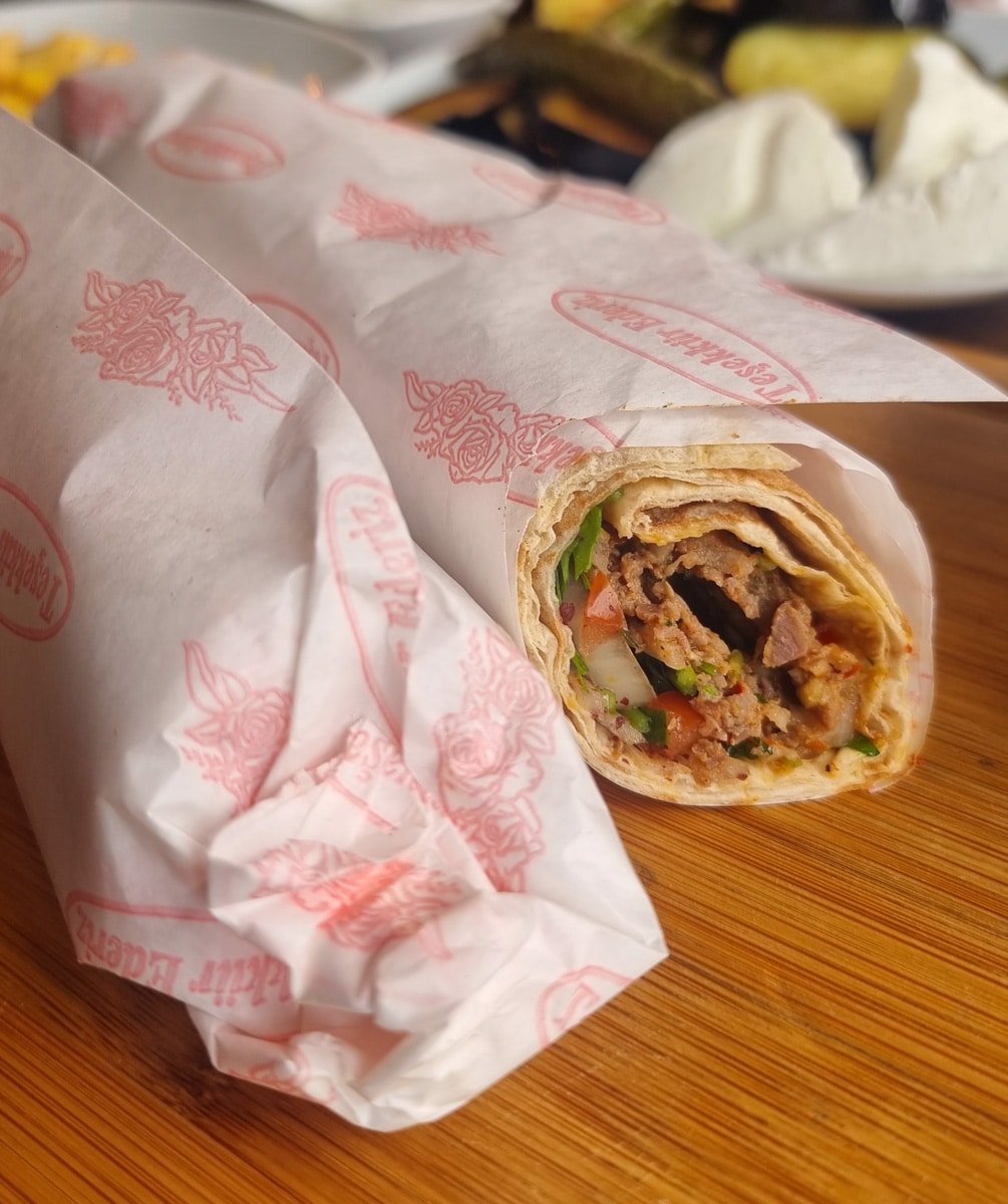 Two wrapped burritos on a wooden table, one partially unwrapped revealing meat, vegetables, and sauce inside—much like the delightful surprises you might uncover exploring local eateries as part of "A Guide to Kadikoy Istanbul.