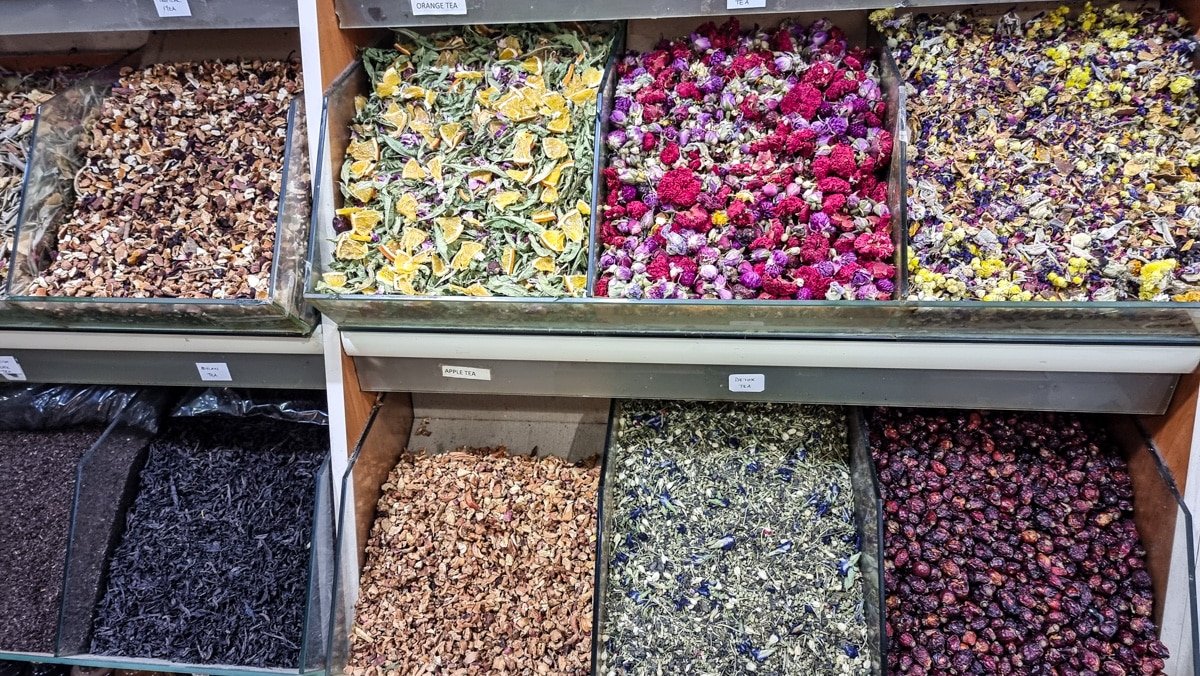 A display of dried herbs, spices, and flowers organized in individual bins at a market—much like those you might find when exploring A Guide To Kadikoy Istanbul. Some bins contain dried oranges, rose petals, and mixed herbs.