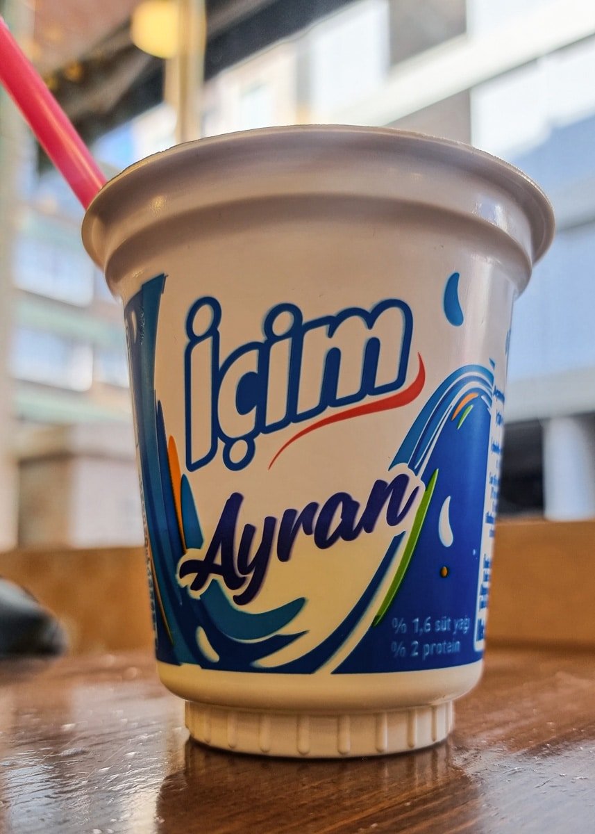 A cup of İçim Ayran on a table, featuring the brand logo and nutritional information, with a pink straw.
