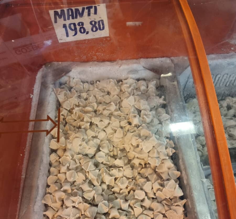 Stack of manti dumplings with a price tag in a glass freezer display at a grocery store.