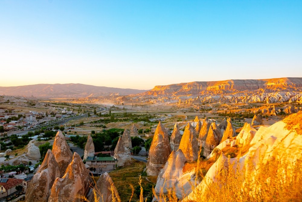Sunset illuminates the unique rock formations and landscape of Cappadocia, Turkey, with a clear blue sky.