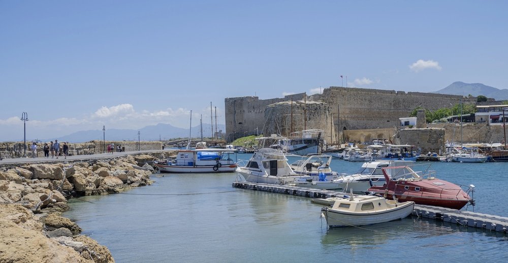 A historic fortress in North Cyprus looms over a calm marina with numerous small boats docked, all under a clear blue sky. To enhance your visit, explore the list of 25 Things To Do nearby.