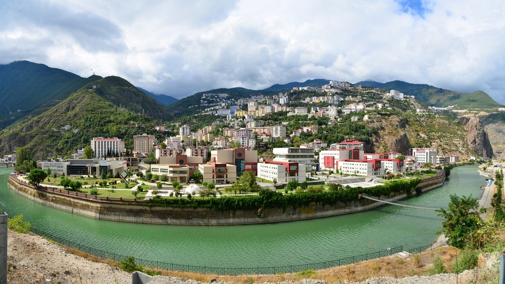 A panoramic view of Artvin Turkey a riverside town with modern buildings on a lush hillside, surrounded by green mountains under a cloudy sky showcases one of the beautiful cities in Turkey.