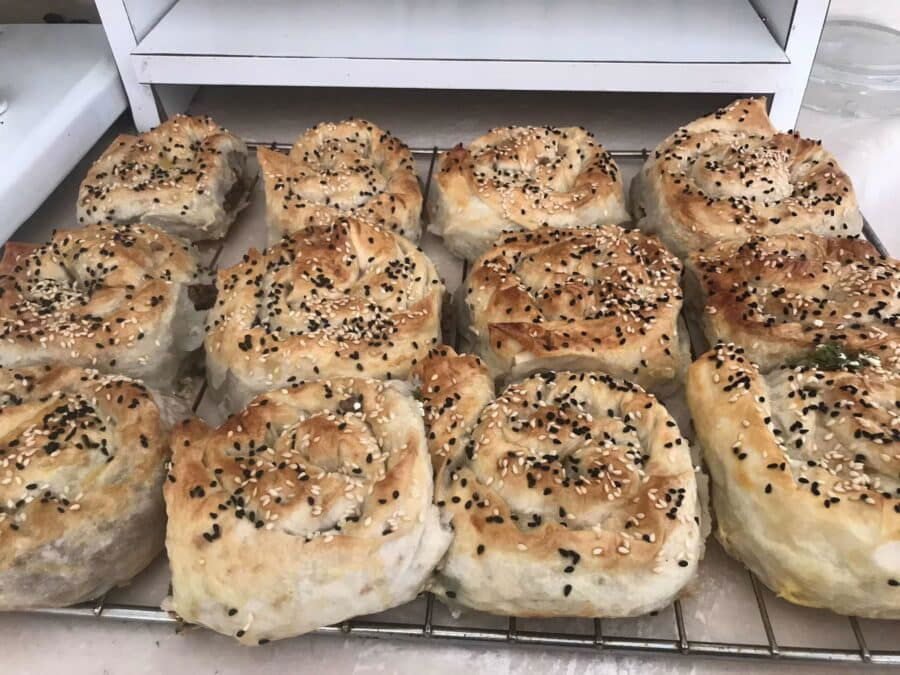 A tray of freshly baked, golden-brown Turkish Borek topped with white and black sesame seeds, cooling on a metal rack.