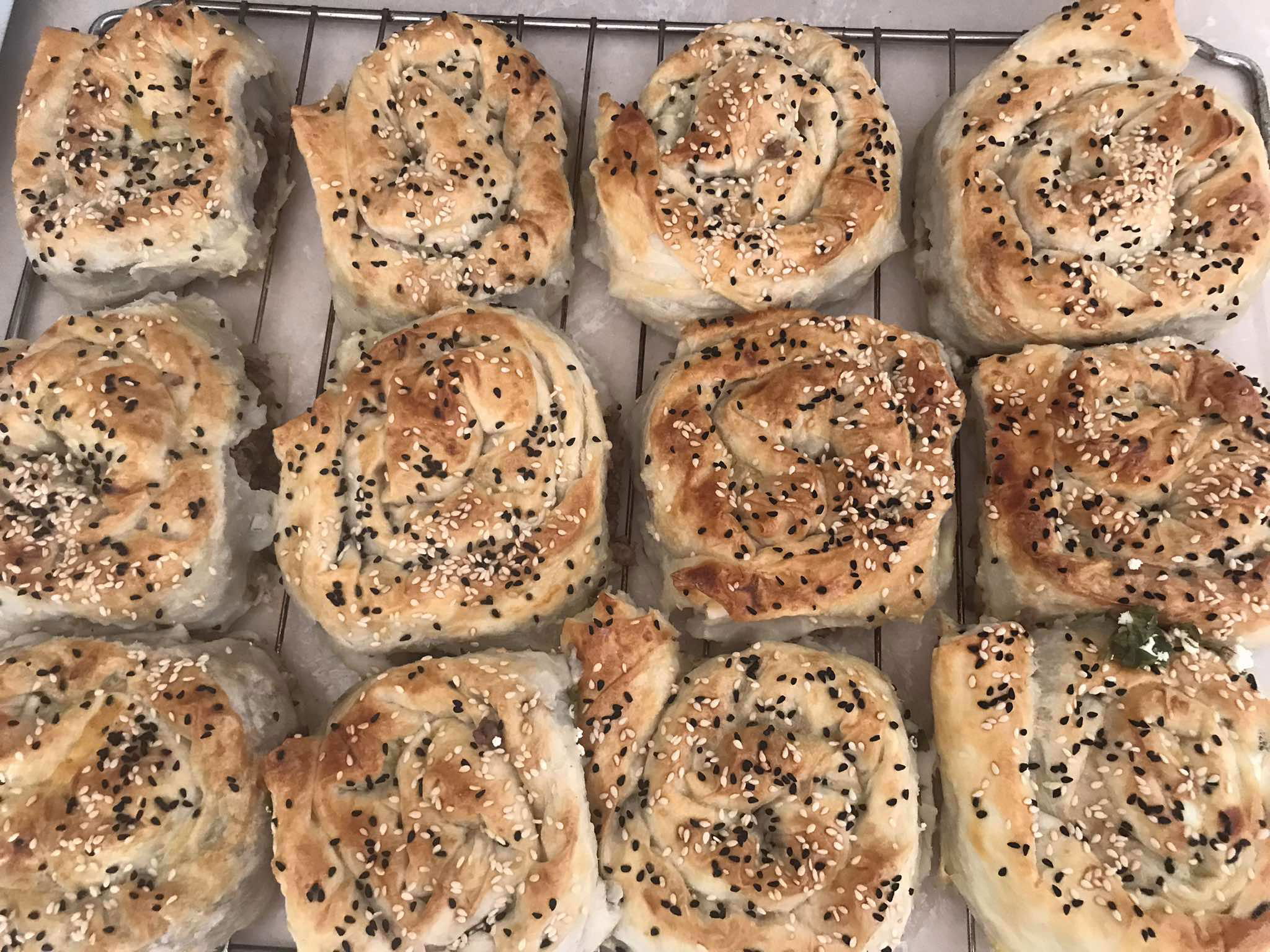 A tray of freshly baked pastry rolls, reminiscent of Turkish Borek, topped with black and white sesame seeds and arranged in a grid pattern.