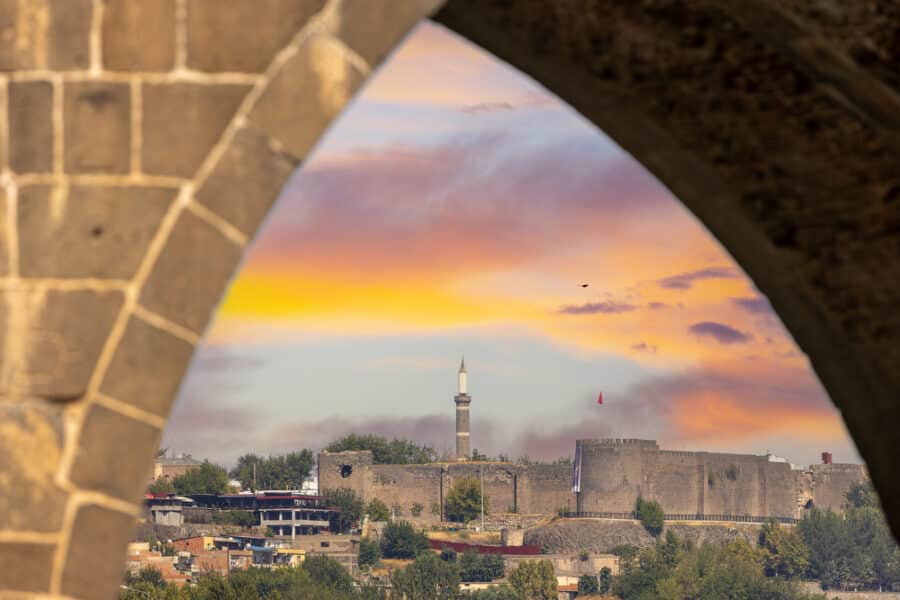 Discover non-touristy places in Turkey perfect for Instagram with this cityscape view framed by an arch, featuring a Diyarbakir under a colorful sunset sky.