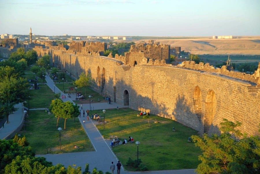 Ancient stone walls stretch along a public park with green lawns and pathways. People are strolling, sitting, and enjoying the open space. The backdrop shows distant buildings and open fields—a perfect spot for capturing Turkey's lesser-known gems on your Travel Instagram.