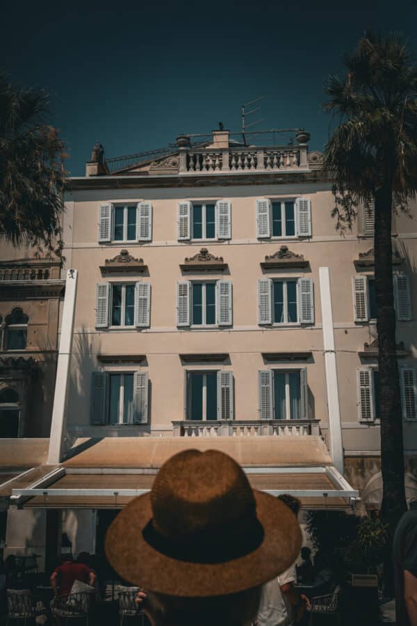 A person in a straw hat looks at a beige building with multiple windows and balconies under a clear, dark sky, pondering Split weather tips for their upcoming visit.