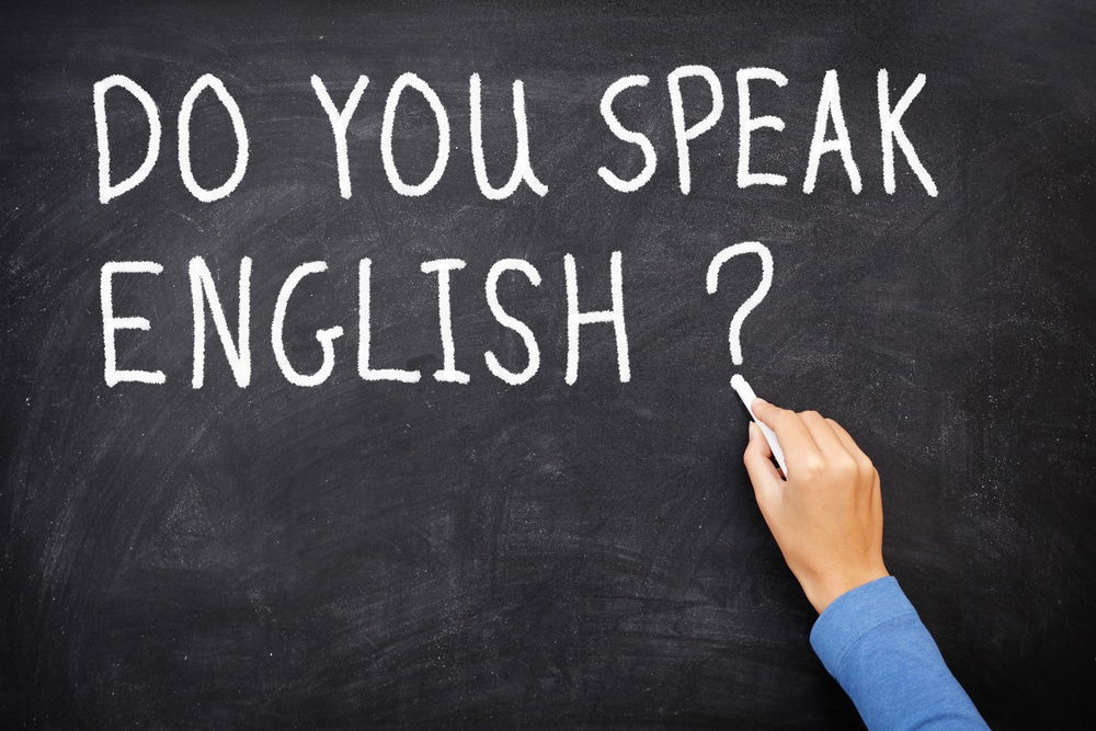 Hand writing "DO YOU SPEAK ENGLISH?" in white chalk on a blackboard, emphasizing the importance of learning English in Turkey.