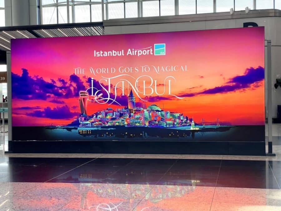 A large digital display at Istanbul Airport showcases a vibrant cityscape alongside the text: "The World Goes to Magical Istanbul," highlighting its role as a key transport hub.