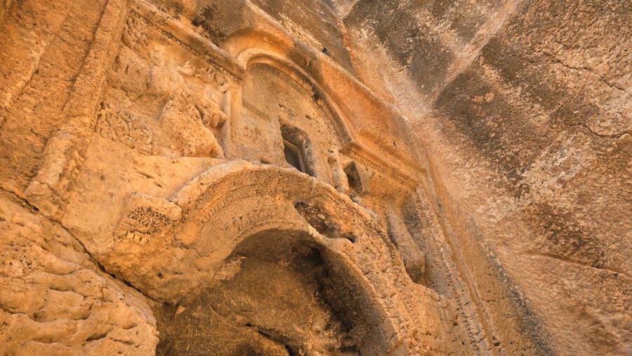 Close-up of an ancient stone arch with intricate carvings, reminiscent of Mesopotamian heritage, set against a rugged wall surface. This stunning piece echoes the architectural elegance found in Mardin, Turkey, showcasing remarkable historical details.